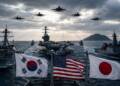 South Korean, US and Japanese flags fly aboard warships as a multinational naval fleet, including an aircraft carrier and destroyers, conducts operations at sea beneath fighter jets and dramatic storm clouds.