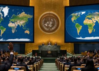 UN General Assembly delegates vote in a formal assembly hall, with large screens displaying contrasting world map projections that highlight differences in the apparent size of Africa and Greenland