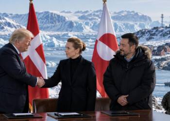 US, Danish and Greenland leaders shake hands during a security agreement signing, with Arctic glaciers, military facilities, naval vessels and national flags in the background.