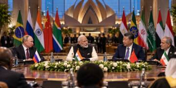 Narendra Modi sits between Vladimir Putin and Xi Jinping at a BRICS summit table, with Iranian President Masoud Pezeshkian beside them and national flags in the background.