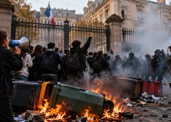 France school protests outside a Paris school, with student demonstrators facing riot police amid smoke, flames, and barricades.